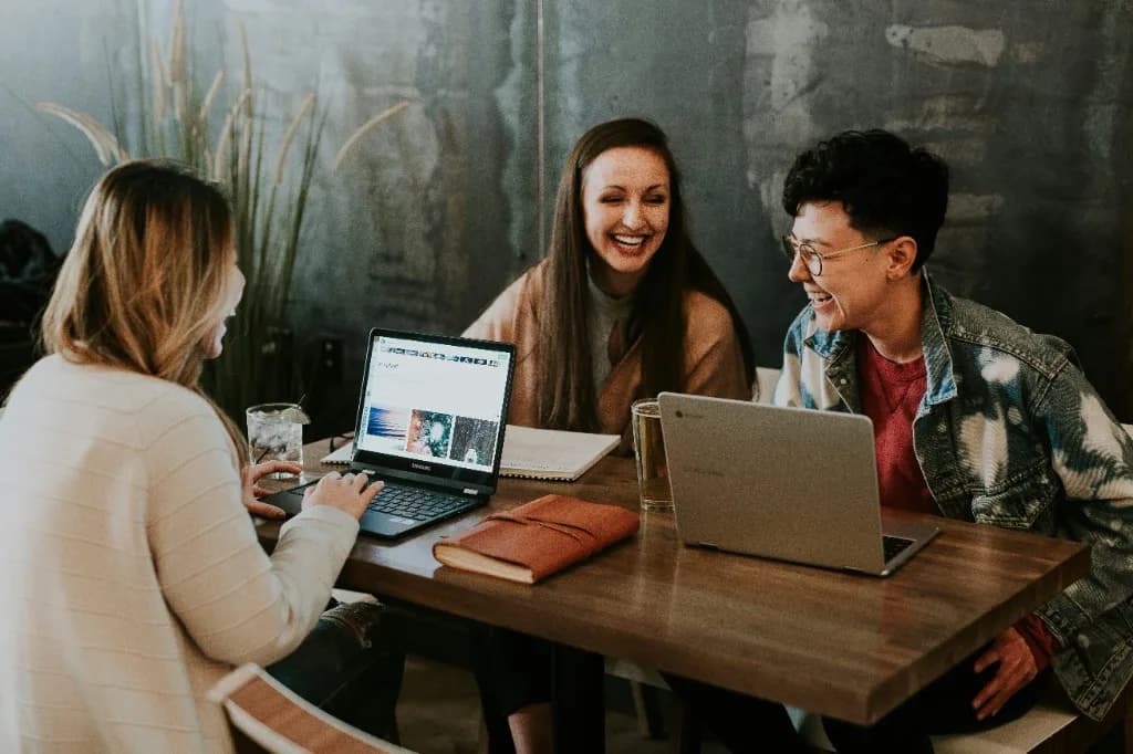 Three people collaborating around laptops at a wooden table